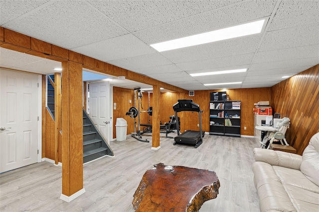 exercise room featuring wooden walls, a drop ceiling, baseboards, and wood finished floors