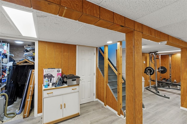 finished basement featuring wooden walls, light wood-type flooring, and a drop ceiling