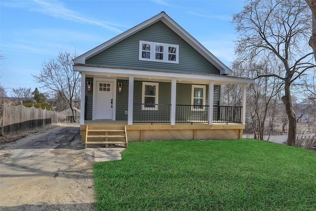 view of front facade with covered porch, driveway, a front yard, and fence