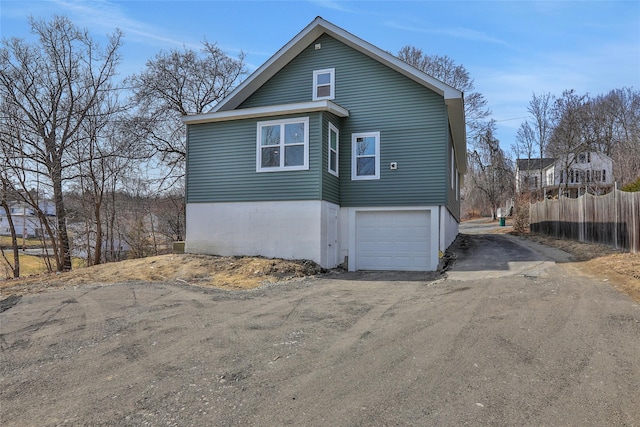 view of side of home with an attached garage, fence, and dirt driveway