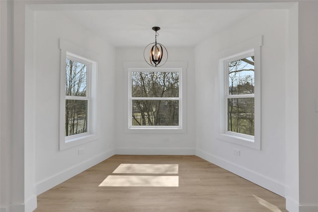 unfurnished dining area featuring baseboards, an inviting chandelier, and light wood finished floors