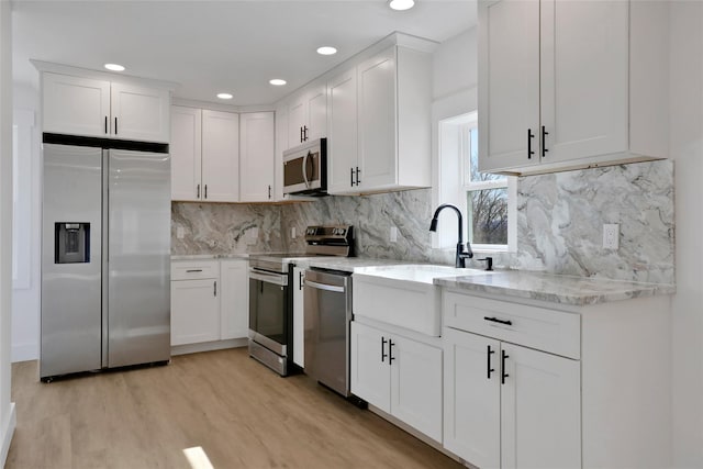 kitchen featuring light stone counters, a sink, stainless steel appliances, white cabinets, and light wood-style floors