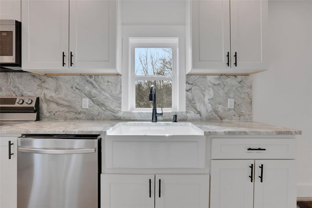 kitchen featuring tasteful backsplash, light stone countertops, appliances with stainless steel finishes, white cabinets, and a sink