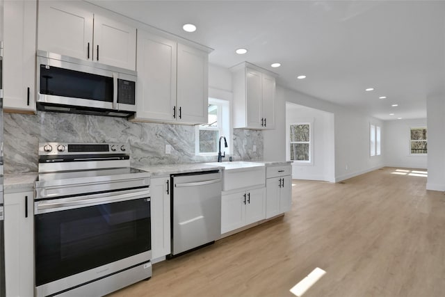 kitchen with light wood-style flooring, a sink, tasteful backsplash, white cabinetry, and appliances with stainless steel finishes