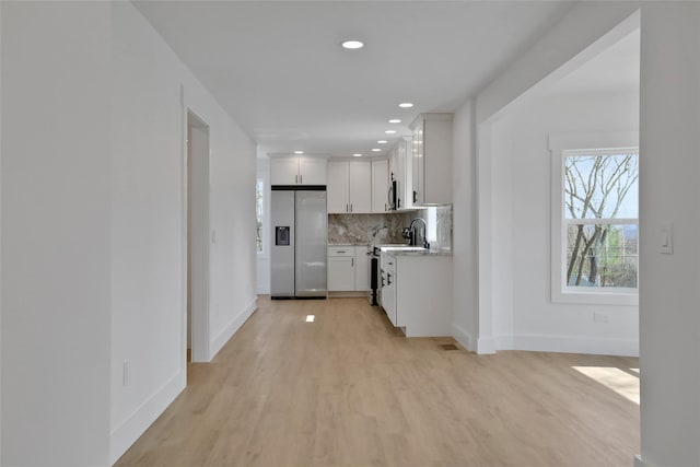 kitchen with backsplash, white cabinetry, stainless steel appliances, light wood finished floors, and baseboards