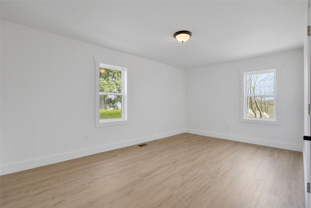 unfurnished room with light wood-style floors, visible vents, a wealth of natural light, and baseboards