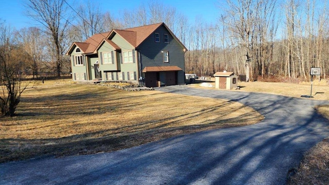 view of side of home featuring an attached garage, a lawn, a storage shed, an outbuilding, and driveway