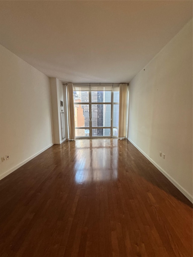 unfurnished room featuring baseboards, dark wood finished floors, and floor to ceiling windows