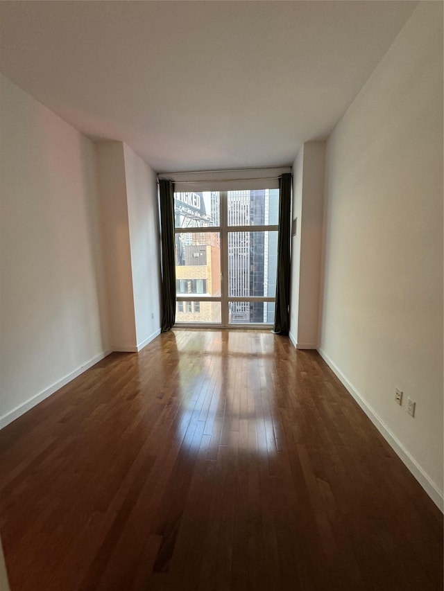 empty room featuring floor to ceiling windows, dark wood-style floors, and baseboards