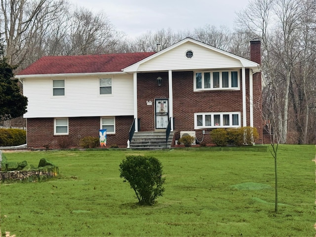 raised ranch featuring brick siding, a chimney, and a front yard