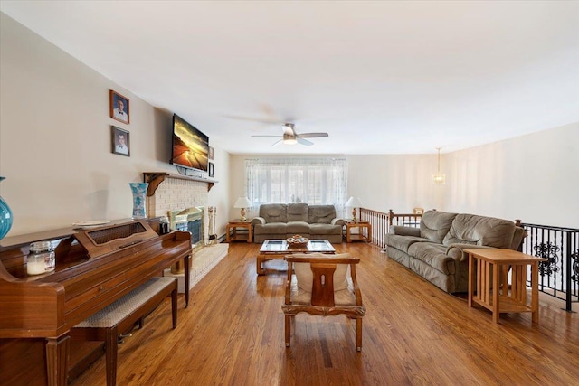 living area with a brick fireplace, wood finished floors, and ceiling fan