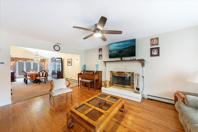 living area with visible vents, a ceiling fan, hardwood / wood-style floors, baseboard heating, and a brick fireplace