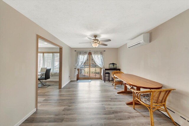 dining space with a baseboard heating unit, an AC wall unit, wood finished floors, and a textured ceiling