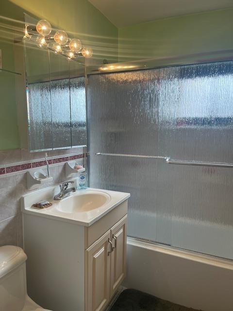 full bathroom with tile walls, bath / shower combo with glass door, toilet, lofted ceiling, and vanity