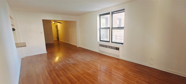 unfurnished room with radiator heating unit, wood finished floors, baseboards, and ceiling fan