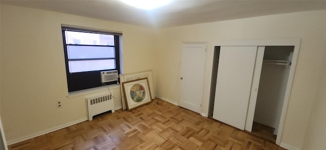 unfurnished bedroom featuring a closet, cooling unit, radiator heating unit, and baseboards