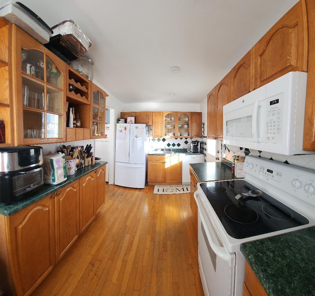 kitchen featuring light wood finished floors, tasteful backsplash, glass insert cabinets, brown cabinetry, and white appliances