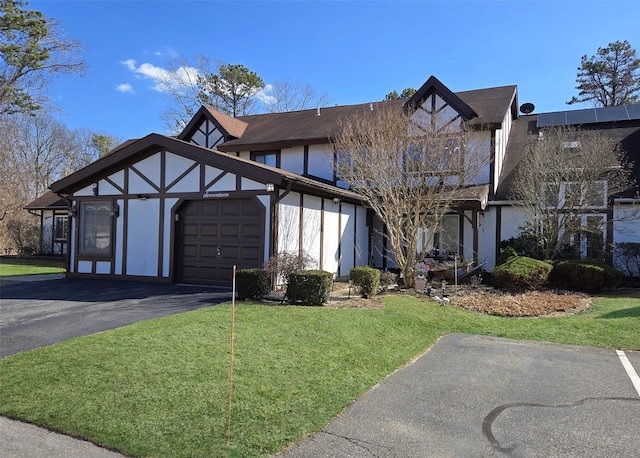 tudor house featuring a garage, a front lawn, driveway, and stucco siding