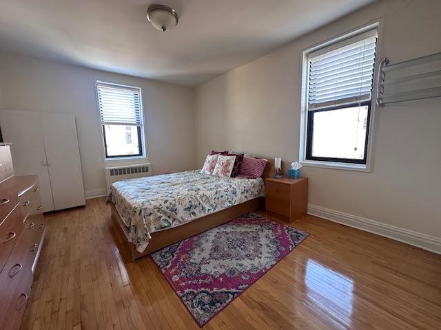 bedroom with radiator heating unit, baseboards, and wood finished floors