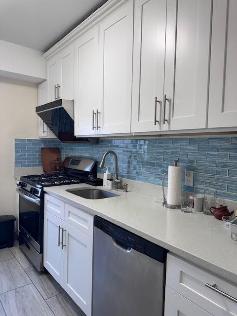 kitchen with a sink, backsplash, appliances with stainless steel finishes, and white cabinetry