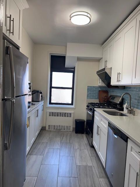 kitchen featuring ventilation hood, radiator heating unit, light countertops, stainless steel appliances, and a sink