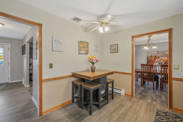 dining room featuring light wood finished floors, visible vents, baseboards, baseboard heating, and ceiling fan with notable chandelier