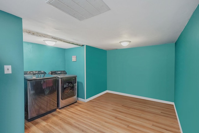 clothes washing area featuring visible vents, wood finished floors, washing machine and dryer, baseboards, and laundry area