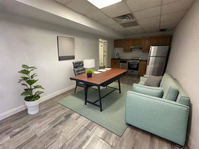 office featuring visible vents, baseboards, a drop ceiling, a sink, and light wood-style floors