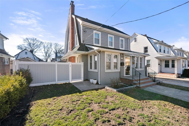 dutch colonial with a front yard, a gate, fence, stucco siding, and a chimney