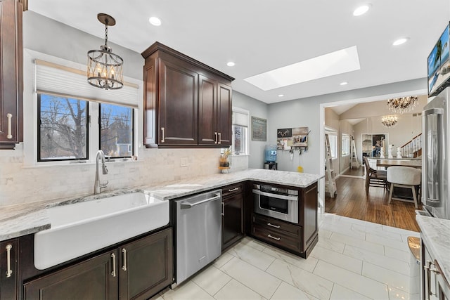 kitchen featuring an inviting chandelier, a peninsula, appliances with stainless steel finishes, and a sink