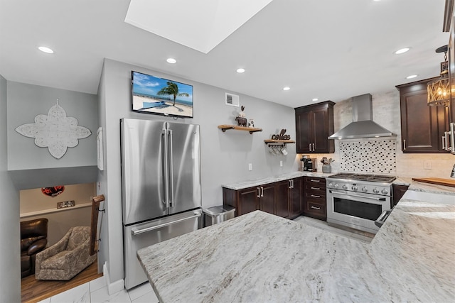 kitchen featuring visible vents, backsplash, wall chimney range hood, dark brown cabinetry, and appliances with stainless steel finishes