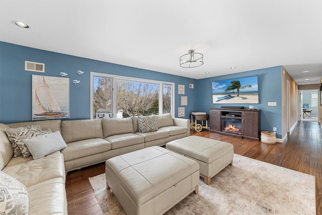 living area with visible vents, a glass covered fireplace, wood finished floors, recessed lighting, and baseboards