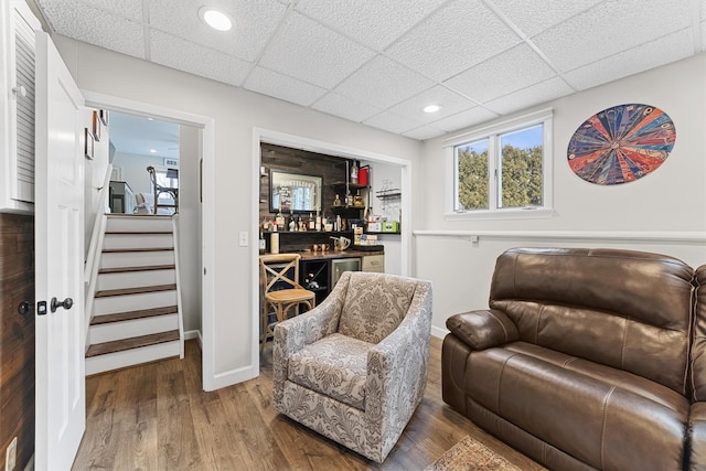 living area with baseboards, stairway, wood finished floors, a bar, and a paneled ceiling