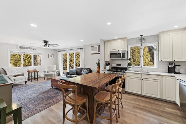 kitchen featuring open floor plan, decorative backsplash, recessed lighting, appliances with stainless steel finishes, and light wood-style floors