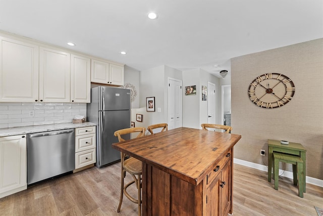 kitchen with light stone counters, recessed lighting, appliances with stainless steel finishes, light wood finished floors, and baseboards