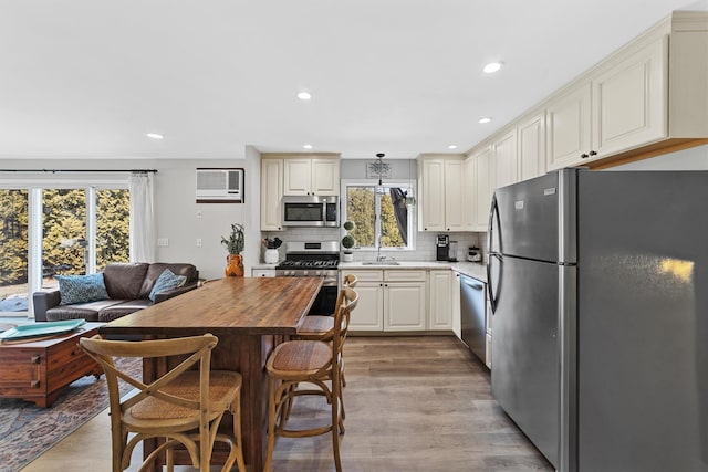 kitchen with wood finished floors, recessed lighting, stainless steel appliances, a wall mounted air conditioner, and tasteful backsplash