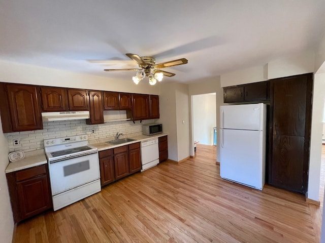 kitchen featuring light wood finished floors, under cabinet range hood, light countertops, white appliances, and a sink