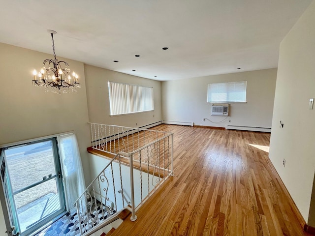 unfurnished living room featuring baseboards, wood finished floors, a notable chandelier, a wall mounted AC, and a baseboard radiator