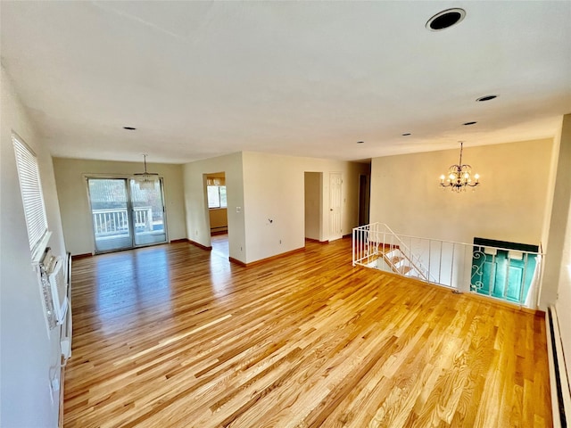 empty room with a baseboard heating unit, baseboards, light wood-type flooring, and a chandelier