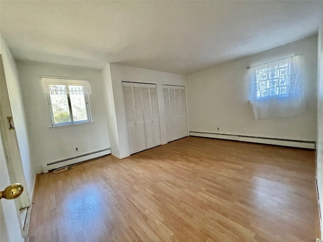 unfurnished bedroom featuring a baseboard heating unit, multiple closets, and wood finished floors