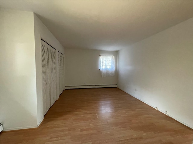 unfurnished bedroom with a closet, baseboard heating, and light wood-type flooring