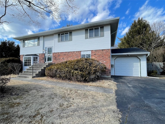 bi-level home with brick siding, an attached garage, driveway, and fence