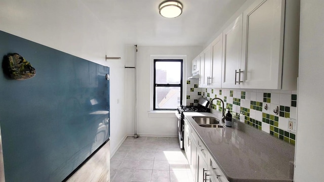 kitchen featuring refrigerator, a sink, stainless steel gas range oven, white cabinetry, and backsplash