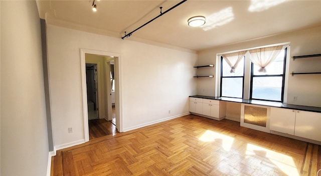 spare room with rail lighting and baseboards