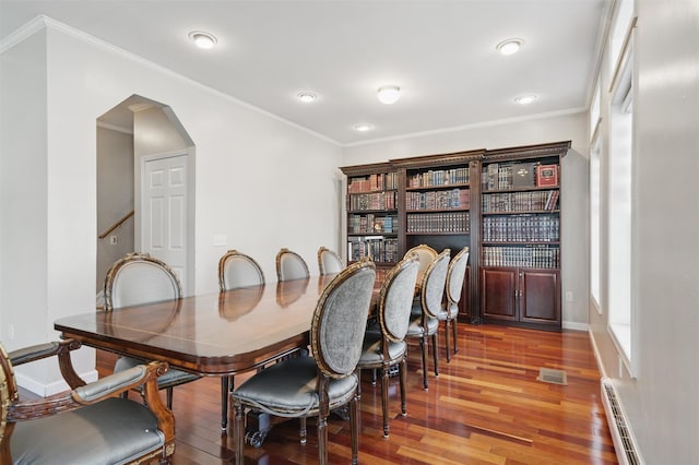 dining area with arched walkways, ornamental molding, baseboard heating, and wood finished floors