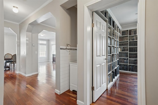 corridor with crown molding, arched walkways, baseboards, and hardwood / wood-style floors
