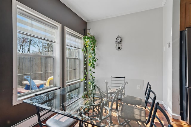 interior space featuring baseboards, a baseboard heating unit, ornamental molding, and wood finished floors