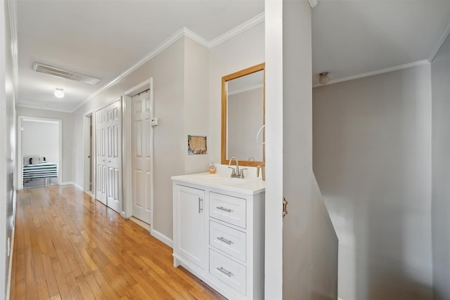 hall with visible vents, a sink, baseboards, ornamental molding, and light wood-style flooring
