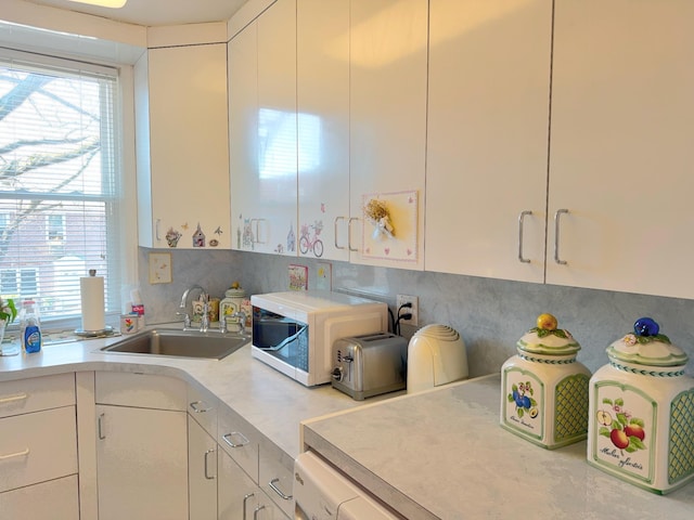 kitchen with a sink, white cabinetry, backsplash, and light countertops