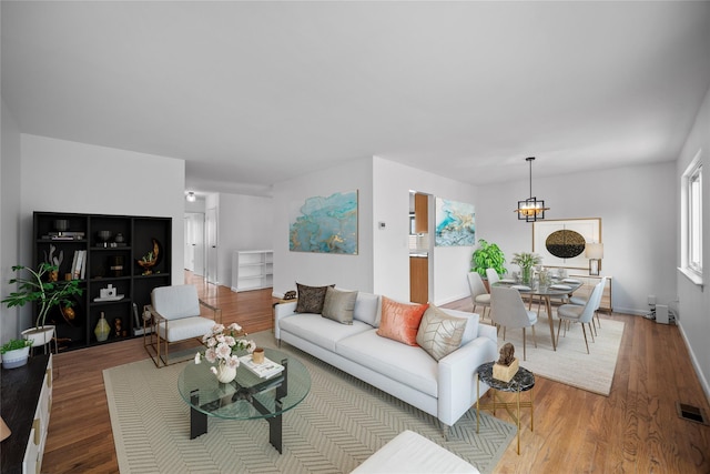 living room with an inviting chandelier, wood finished floors, visible vents, and baseboards